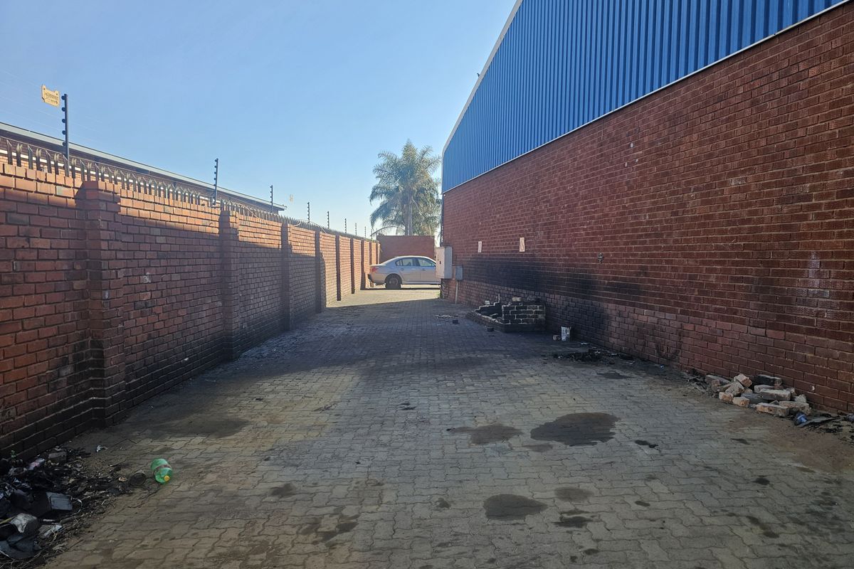 Rear exterior service area featuring brick boundary walls with electric fencing, paved ground surface, and industrial corrugated metal wall cladding.