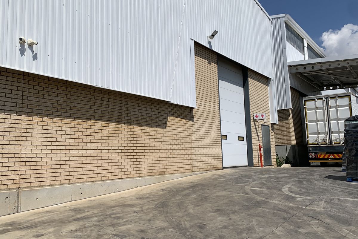 Industrial warehouse exterior featuring a large roller shutter door, brick and metal cladding, and a concrete loading apron.