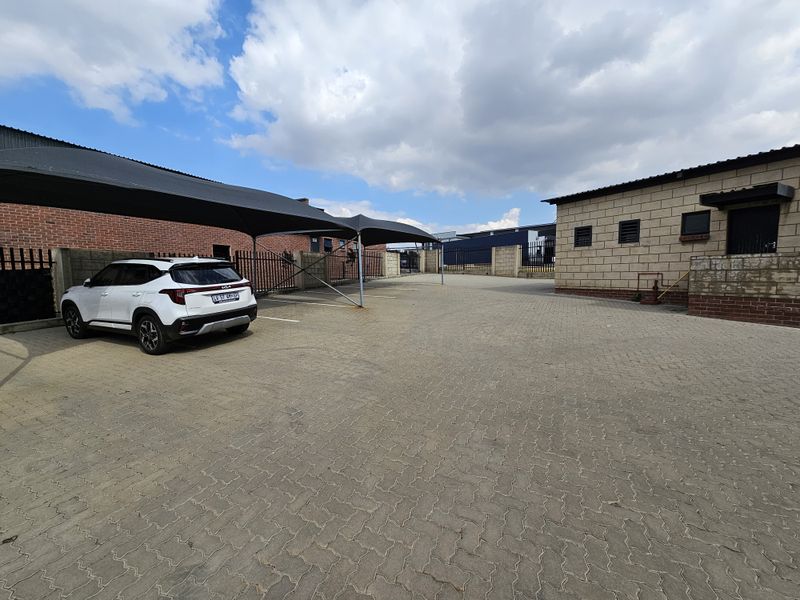 Industrial property exterior featuring a paved parking area with shade cloth carports and secure perimeter walling.