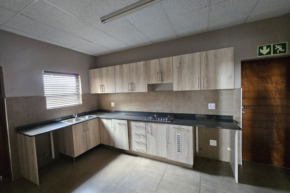 A functional industrial-style kitchen featuring light wood-finish cabinetry, dark laminate countertops, a gas hob, and tiled backsplash with neutral floor tiles.