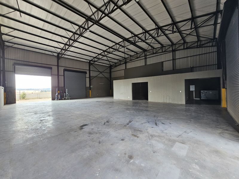 Spacious industrial warehouse featuring high ceilings with exposed steel trusses, concrete flooring, and multiple roller shutter doors for efficient access.