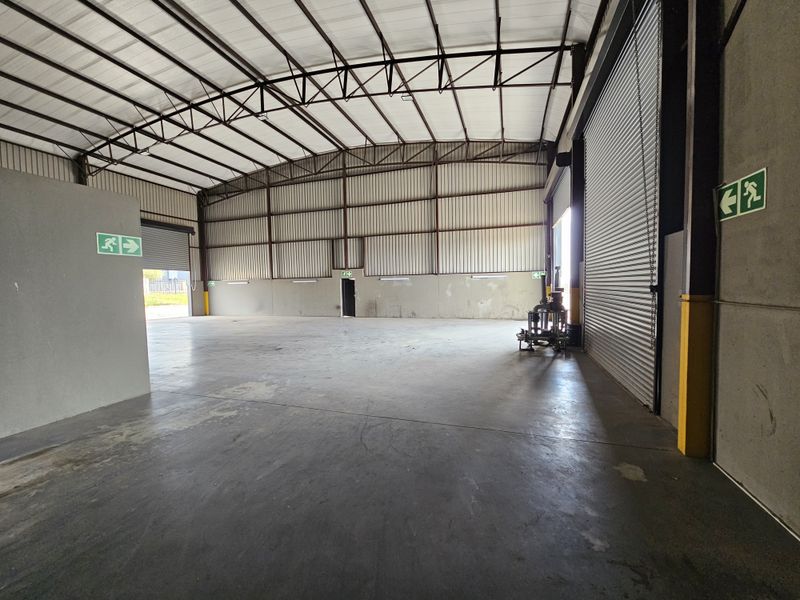 Spacious industrial warehouse unit featuring high-clearance steel truss roofing, concrete flooring, and large roller shutter access doors.
