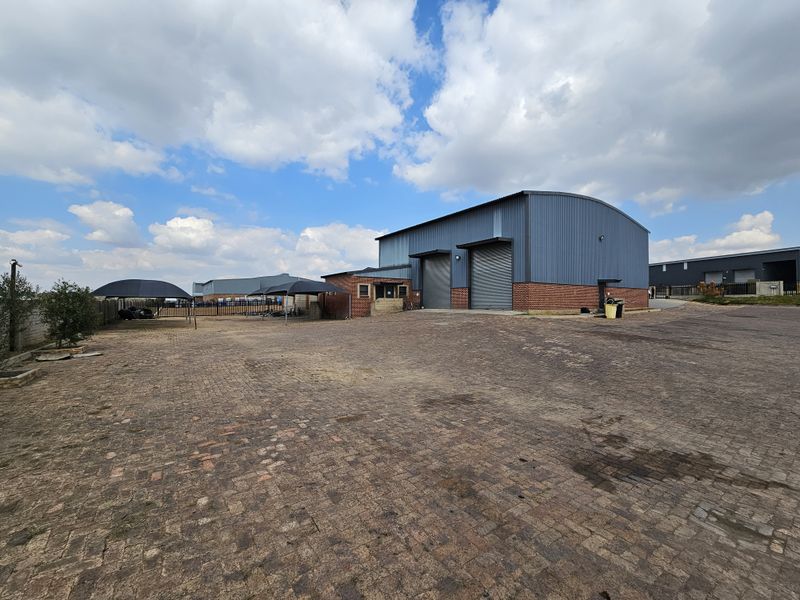 Industrial property featuring a large paved yard, metal-clad warehouse structure with roller shutter doors, and secure perimeter fencing.