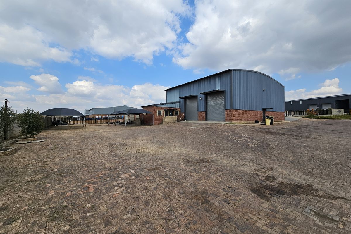 Industrial property featuring a large paved yard, metal-clad warehouse structure with roller shutter doors, and secure perimeter fencing.