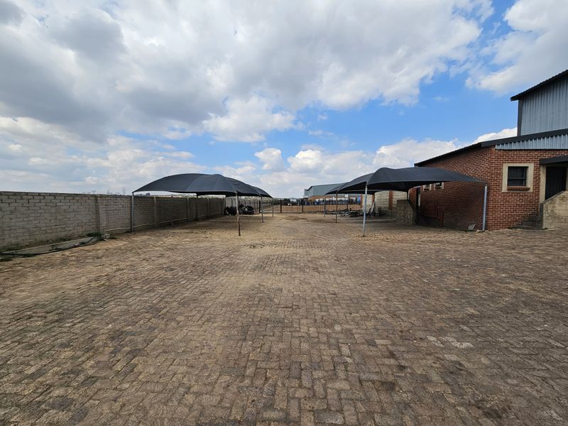 Spacious paved industrial yard featuring multiple shade cloth carports, enclosed by a perimeter brick wall and metal gate.