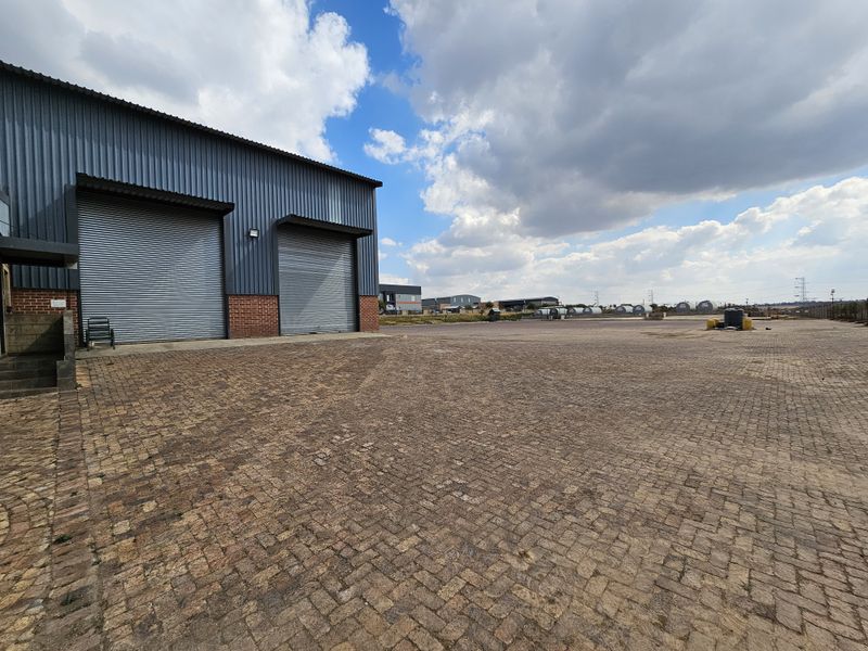 Industrial property featuring a large paved yard area with two roller shutter doors and corrugated metal cladding exterior.