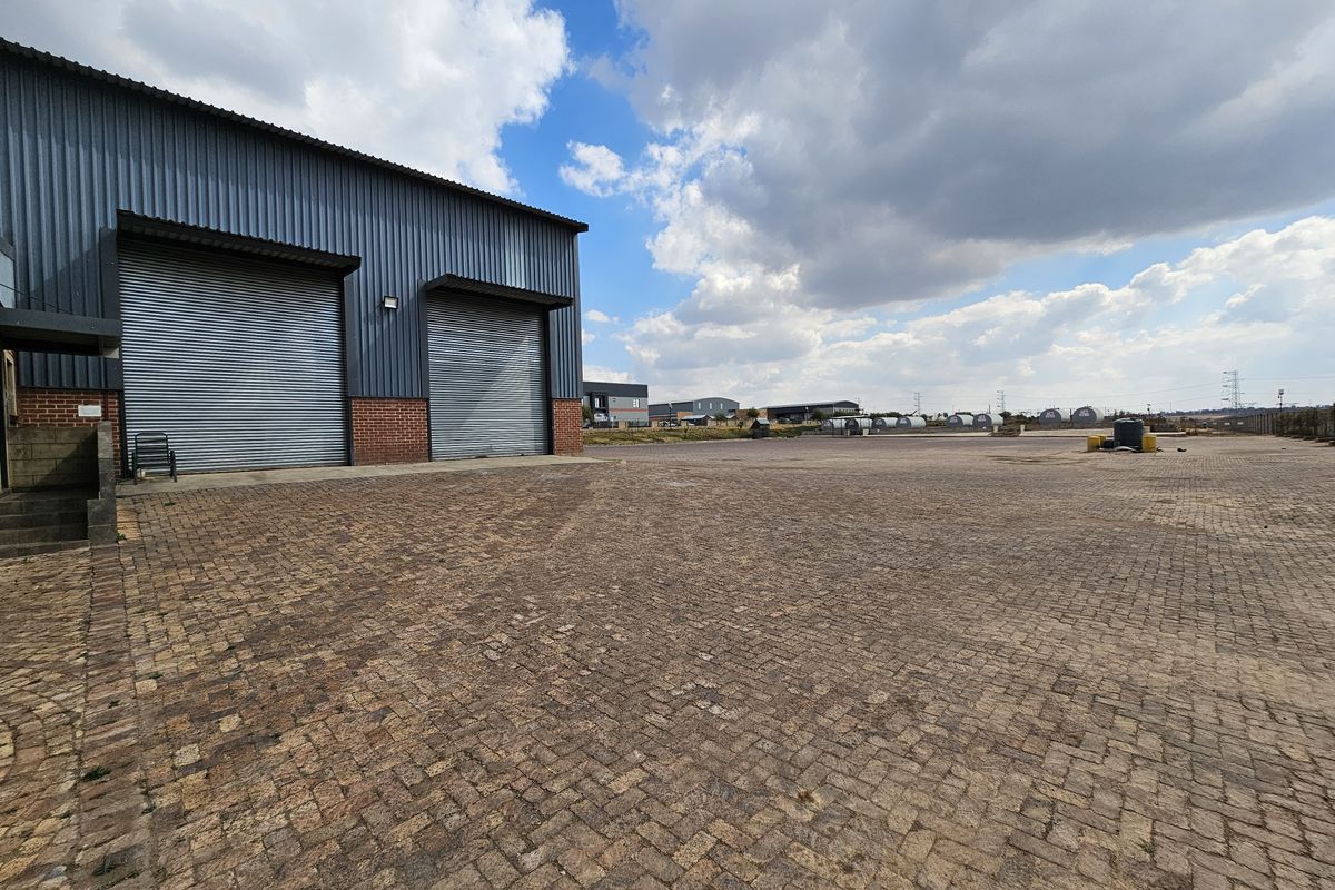 Industrial property featuring a large paved yard area with two roller shutter doors and corrugated metal cladding exterior.