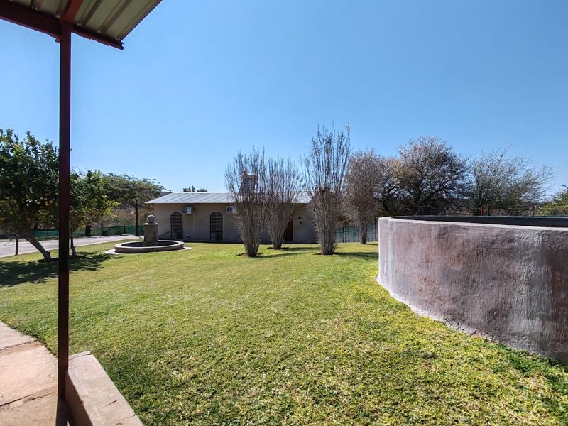 A spacious rear garden featuring a manicured lawn, a decorative water fountain, and a large concrete water reservoir, viewed from a covered patio area.