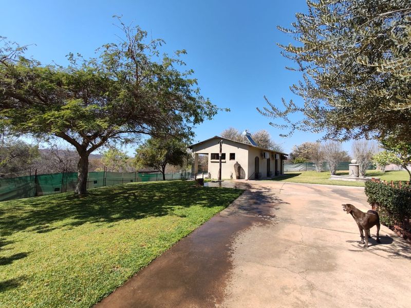 A view of the rear exterior of the farm property, featuring a concrete driveway, well-maintained lawn, and a solar water heating system.