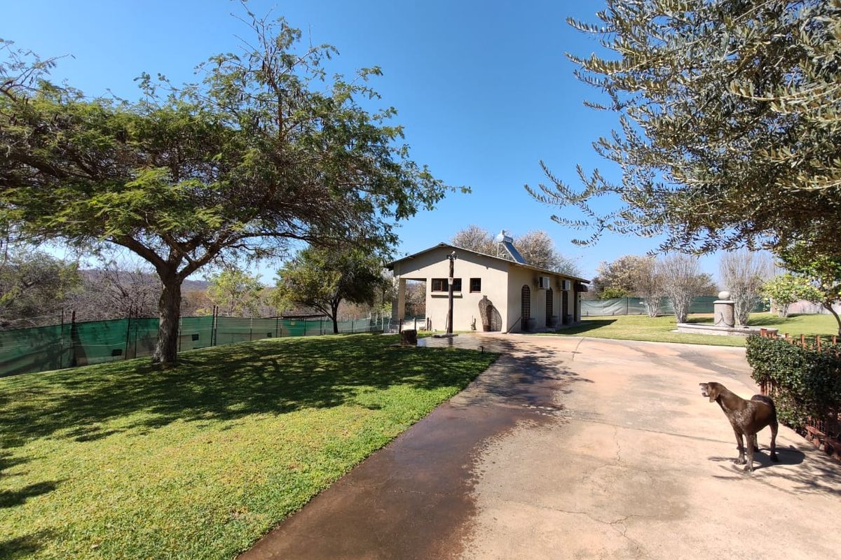 A view of the rear exterior of the farm property, featuring a concrete driveway, well-maintained lawn, and a solar water heating system.
