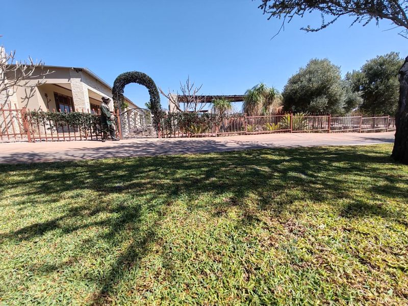 Front view of the property featuring a well-maintained lawn, paved driveway, and decorative metal fencing with an arched entrance gate.