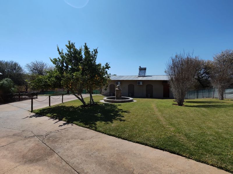Rear view of the farm property featuring a landscaped garden, stone fountain, concrete driveway, and solar water heating system on the roof.