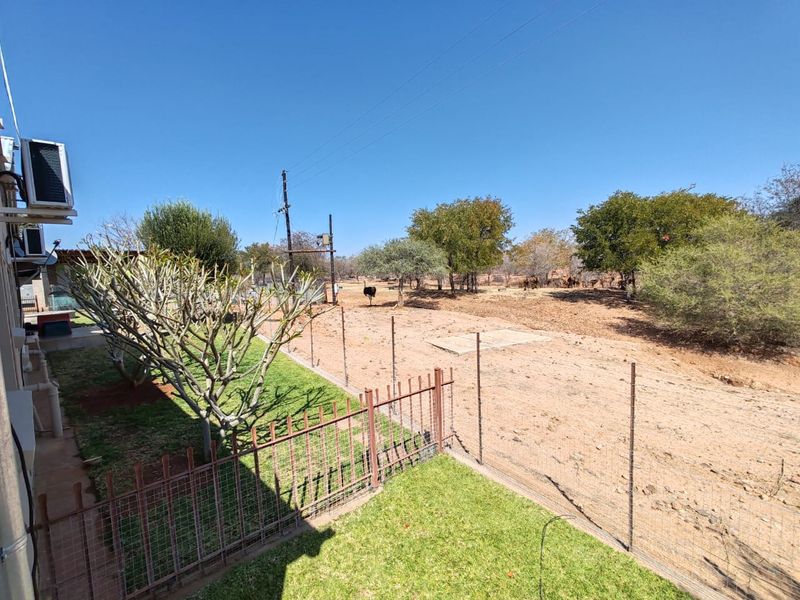 A view of the rear yard featuring wire mesh fencing, a small lawn area, and open farm land with mature trees.