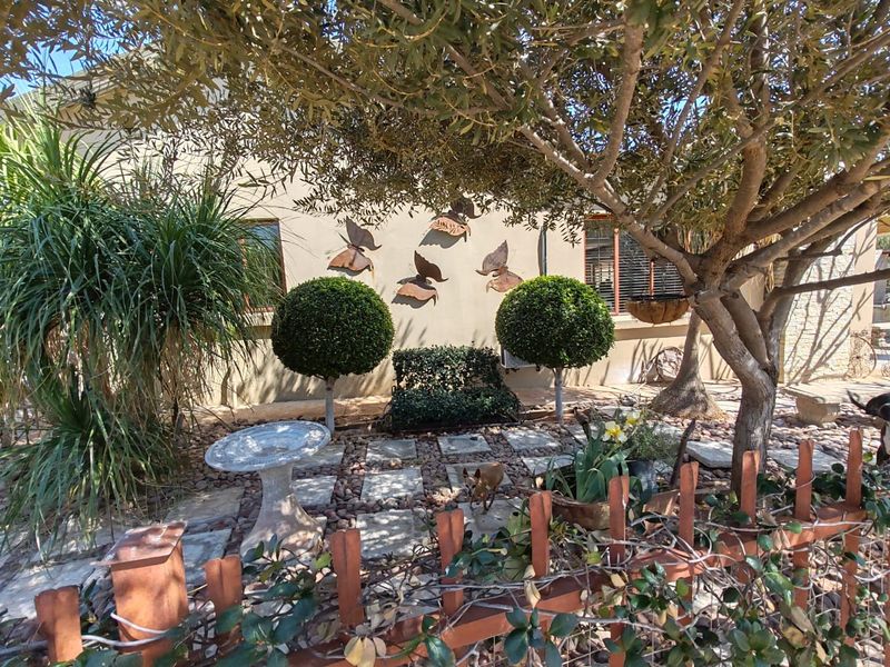 A well-maintained garden area featuring stone paving, mature trees, and decorative metal fencing, providing a pleasant outdoor space.