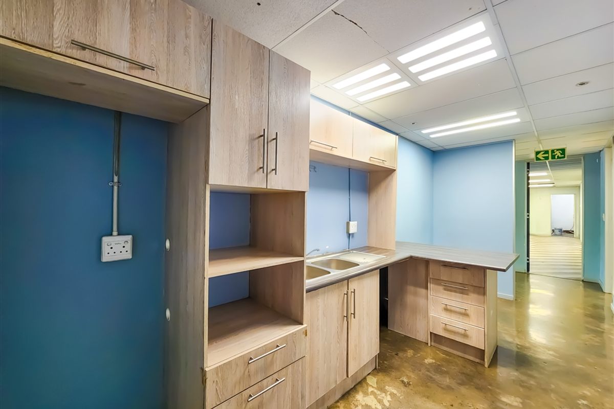 A functional office kitchenette area featuring light wood-finish cabinetry, a stainless steel sink, and integrated storage, set within a professional office environment.