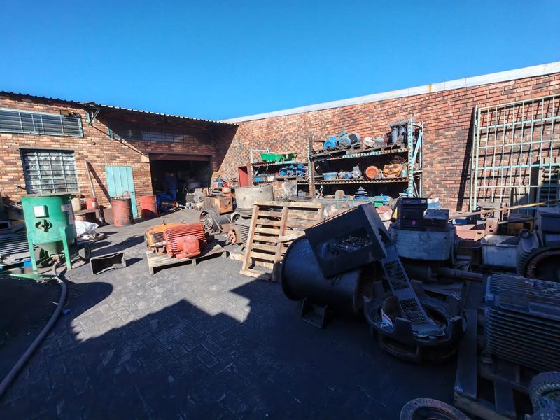 Industrial rear yard area featuring exposed brick walls, paved flooring, and heavy-duty industrial shelving units suitable for storage or workshop operations.