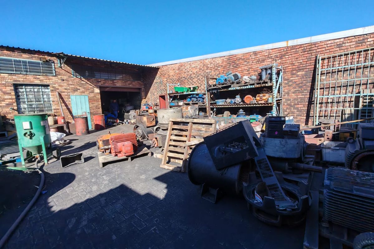 Industrial rear yard area featuring exposed brick walls, paved flooring, and heavy-duty industrial shelving units suitable for storage or workshop operations.