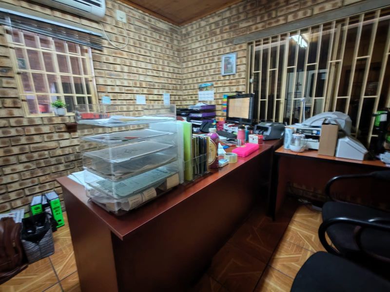 Functional office space featuring exposed brick walls, tiled flooring, timber ceiling, and security bars on windows, equipped with a wall-mounted air conditioning unit.