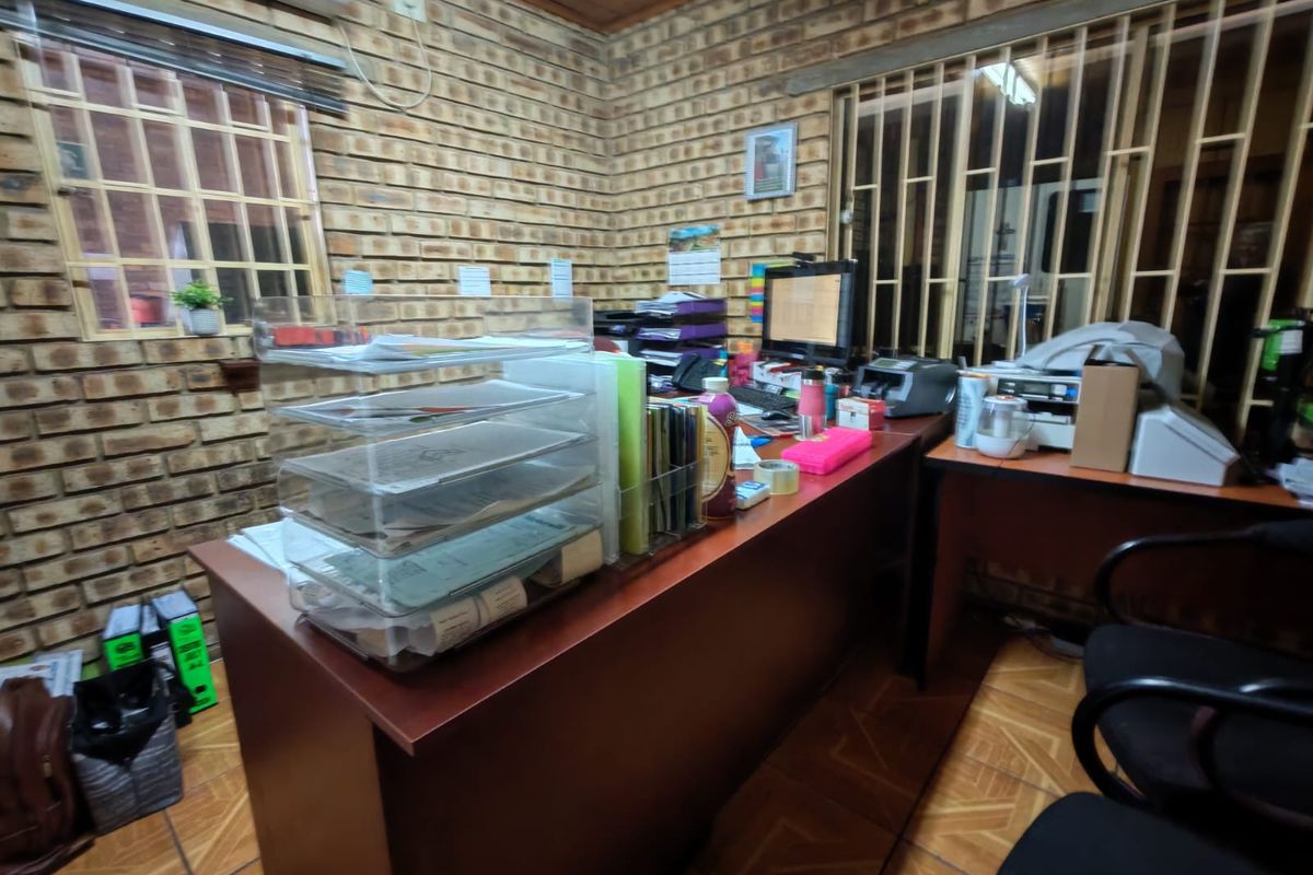 Functional office space featuring exposed brick walls, tiled flooring, timber ceiling, and security bars on windows, equipped with a wall-mounted air conditioning unit.