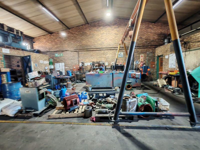 Industrial workshop space featuring exposed brick walls, concrete flooring, and an overhead gantry crane, suitable for heavy-duty manufacturing or maintenance operations.