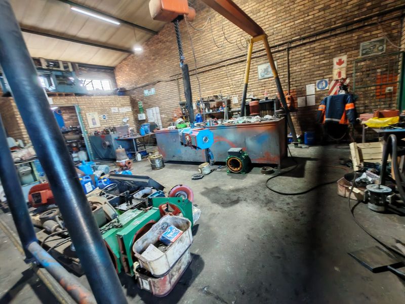 Industrial workshop space featuring exposed brick walls, concrete flooring, and an overhead gantry crane, suitable for heavy-duty manufacturing or repair operations.