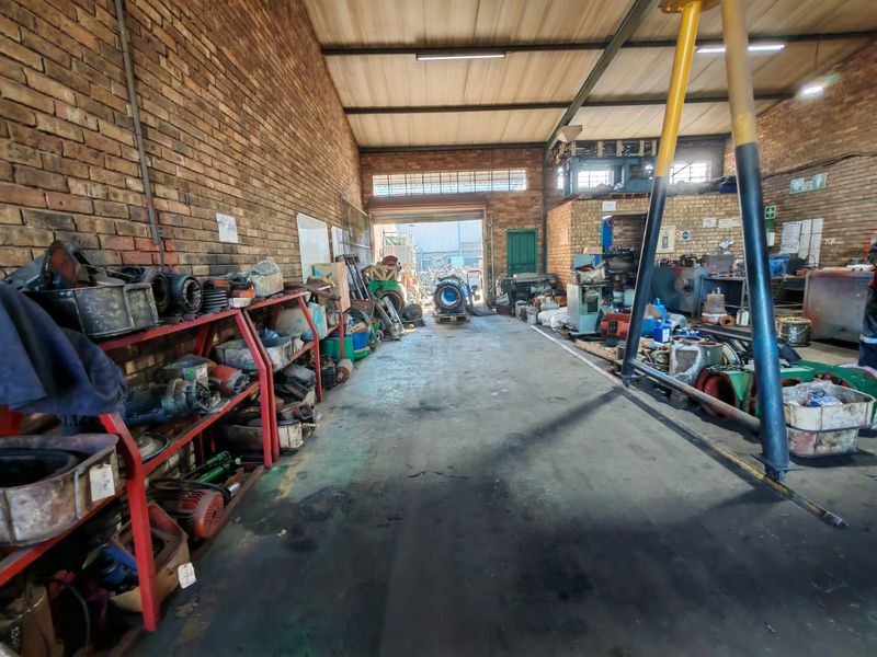 Industrial workshop space featuring exposed brick walls, concrete flooring, and high-clearance metal roofing, suitable for heavy-duty operations or storage.