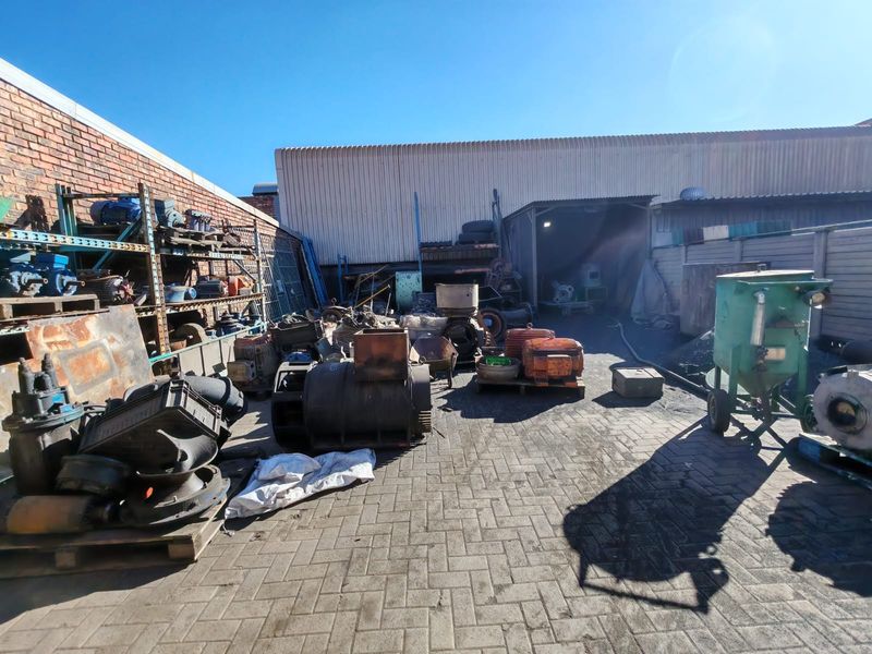 Industrial rear yard area featuring paved ground, brick boundary walls, and corrugated metal cladding, currently utilized for storage of industrial equipment and machinery.
