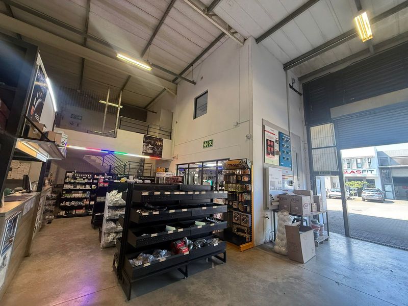 Industrial warehouse space featuring high ceilings with exposed steel trusses, a mezzanine level, concrete flooring, and a large roller shutter door for easy access.
