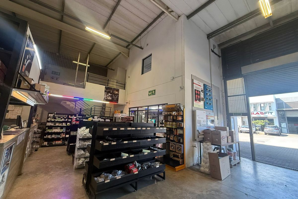 Industrial warehouse space featuring high ceilings with exposed steel trusses, a mezzanine level, concrete flooring, and a large roller shutter door for easy access.