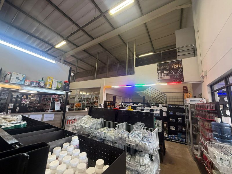 Spacious industrial warehouse interior featuring a mezzanine level, metal staircase, and high-clearance exposed steel roof trusses, currently utilized as a retail trade counter.