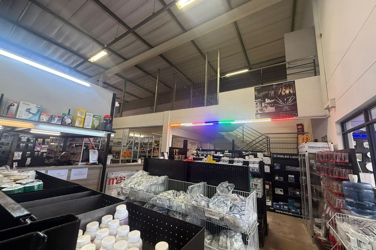 Spacious industrial warehouse interior featuring a mezzanine level, metal staircase, and high-clearance exposed steel roof trusses, currently utilized as a retail trade counter.