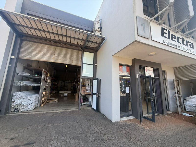 Industrial unit exterior featuring a large roller shutter door, glass storefront entrance, and paved driveway access.