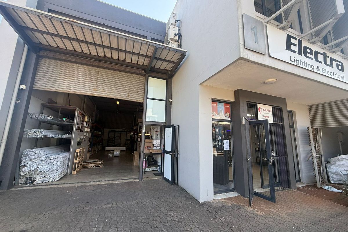 Industrial unit exterior featuring a large roller shutter door, glass storefront entrance, and paved driveway access.