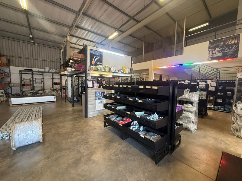 Spacious industrial warehouse interior featuring high ceilings with exposed steel trusses, concrete flooring, and a mezzanine level with staircase access.