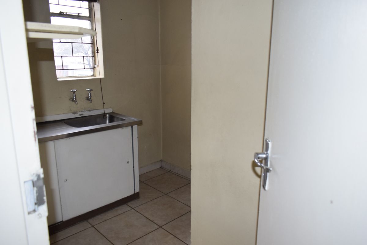 A compact, empty kitchen area featuring a stainless steel sink, base cabinetry, and tiled flooring, suitable for a small office kitchenette.