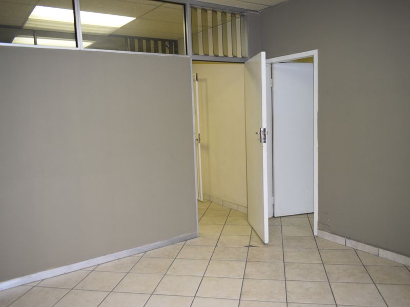 An empty office space featuring tiled flooring, neutral painted walls, and a suspended ceiling with integrated lighting.