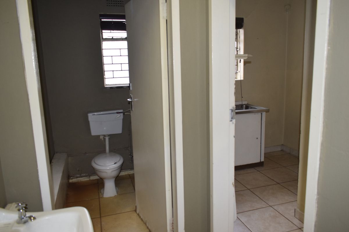 A functional bathroom and adjacent kitchenette area featuring basic sanitary ware, tiled flooring, and simple cabinetry, requiring cosmetic updates.