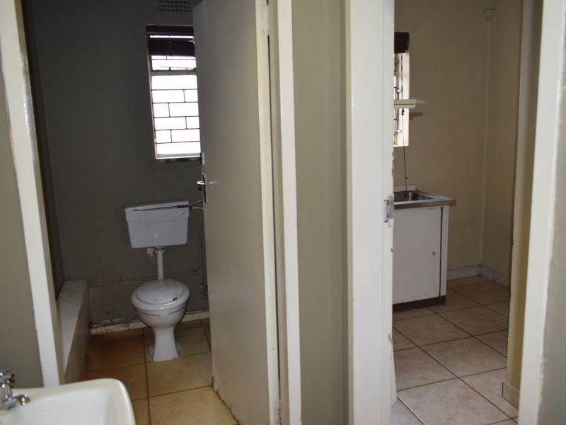 A functional bathroom and adjacent kitchenette area featuring basic sanitary ware, tiled flooring, and simple cabinetry, requiring cosmetic updates.