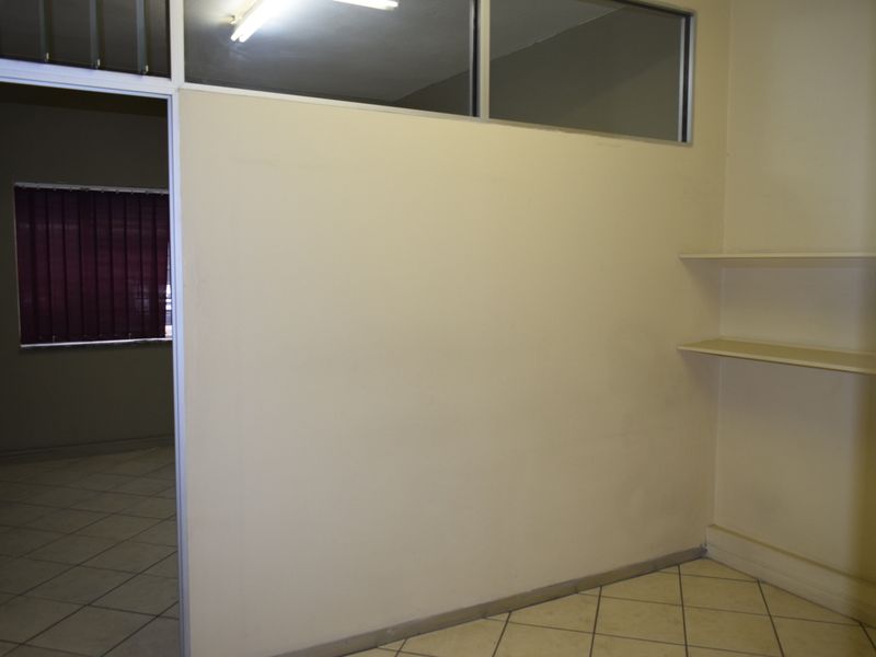 A vacant office space featuring a partition wall with a transom window, built-in shelving, and ceramic tiled flooring.