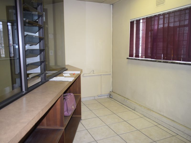 A functional office space featuring a built-in reception counter, tiled flooring, and security-fitted windows, suitable for a professional workspace.