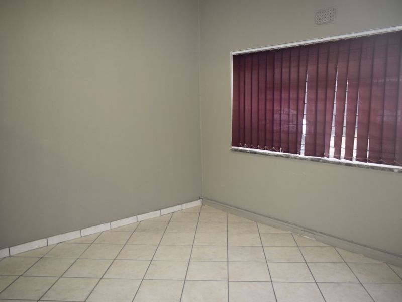 A vacant office space featuring neutral wall tones, tiled flooring, and a window fitted with vertical blinds.