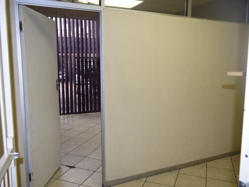 An empty office space featuring partition walls, tiled flooring, and vertical blinds, suitable for a professional workspace setup.