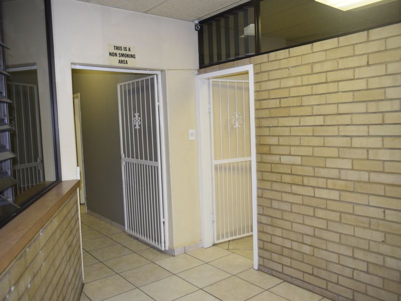 A functional office hallway featuring tiled flooring, exposed brick walls, and secure metal gates leading to separate office or utility spaces.