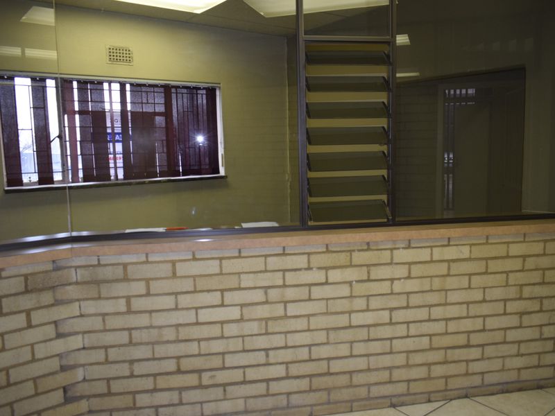 A vacant office reception area featuring a brick counter, glass partition, and louvered windows, offering a functional space for administrative or client-facing operations.