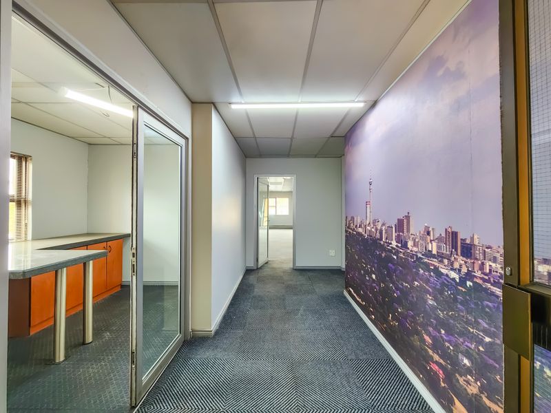 A functional office hallway featuring a glass partition, fitted cabinetry, and a large wall mural, leading to an open office space.