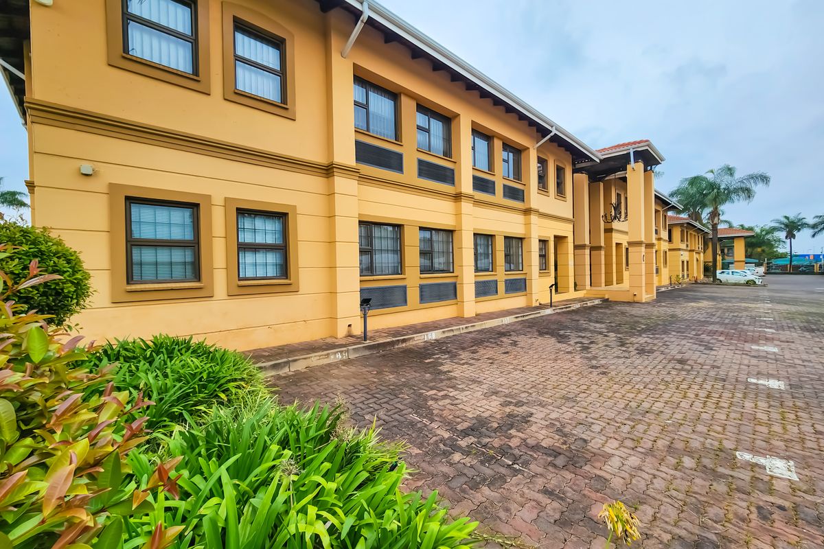A multi-story office building exterior featuring a paved parking area, yellow facade, and multiple casement windows.