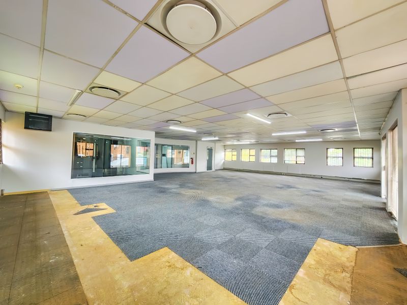 Spacious open-plan office area featuring a suspended ceiling, recessed lighting, and glass partitioning, currently requiring flooring repairs and general refurbishment.
