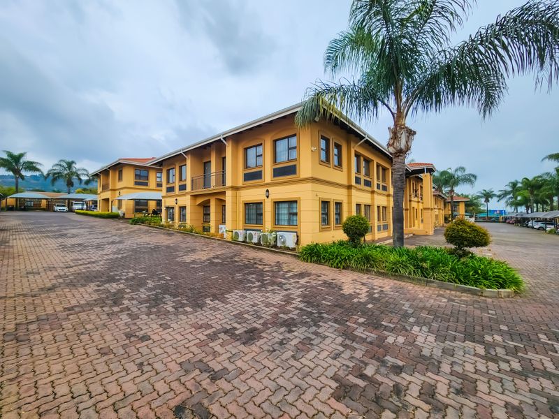 A multi-story office building featuring a paved driveway, external air conditioning units, and a balcony, set within a well-maintained commercial property.