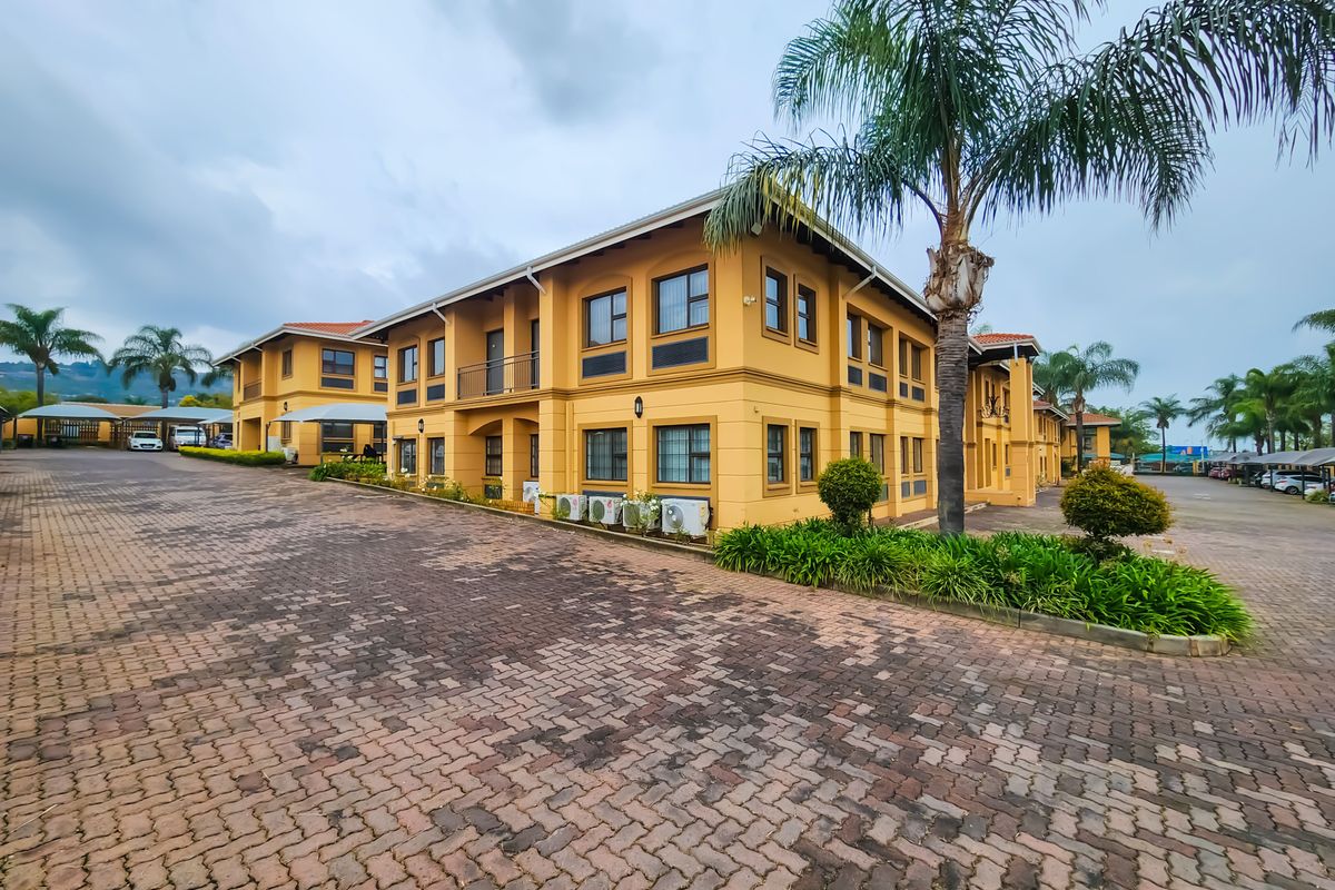 A multi-story office building featuring a paved driveway, external air conditioning units, and a balcony, set within a well-maintained commercial property.