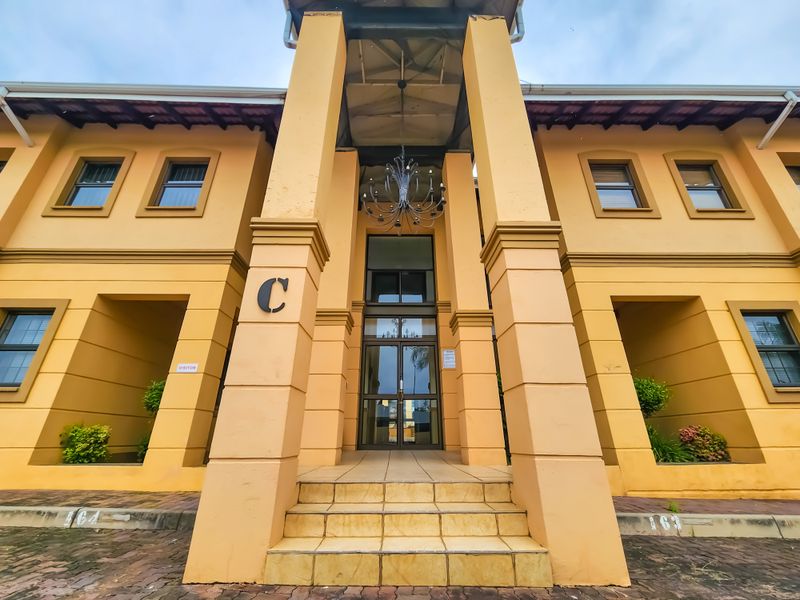 Front facade of office building block C, featuring a covered entrance with prominent pillars, glass door access, and paved visitor parking area.